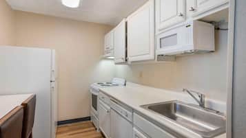 A compact kitchen with white cabinets, a built-in microwave, a stainless steel sink, and a stove.