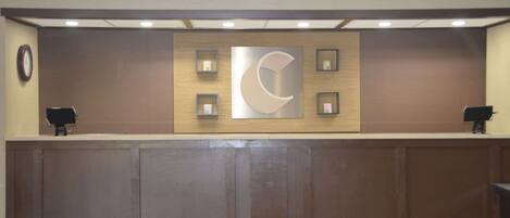 A reception desk with a wooden panel wall, a large crescent moon logo, and two small framed pictures.