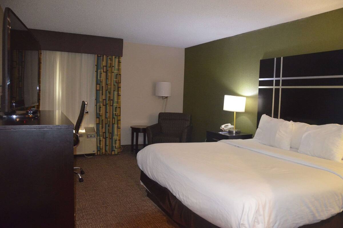 A hotel room with a large bed, a desk with a lamp, a chair, and a television.