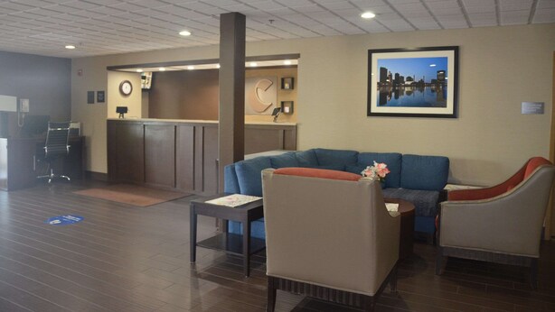A reception area with a blue sofa, a small table, and a chair. There is a clock on the wall and a framed picture above the sofa. - Comfort Inn & Suites Maumee - Toledo (I80-90) (Maumee)