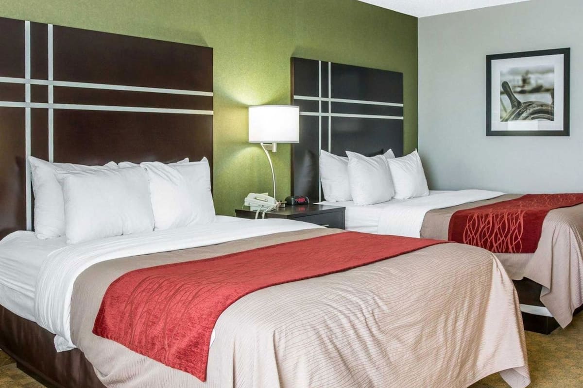 A hotel room with two beds, a nightstand, a lamp, and a framed picture on the wall.