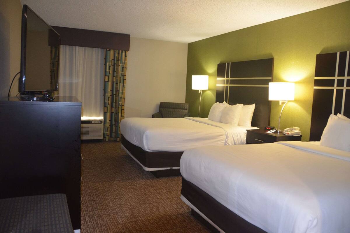 A hotel room with two beds, a desk, a chair, a TV, and a lamp.