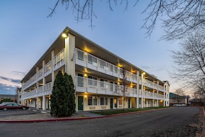 Un hotel de varios pisos con balcones, un estacionamiento y un cielo despejado.