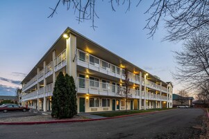 Un hotel de varios pisos con balcones, un estacionamiento y un cielo despejado.