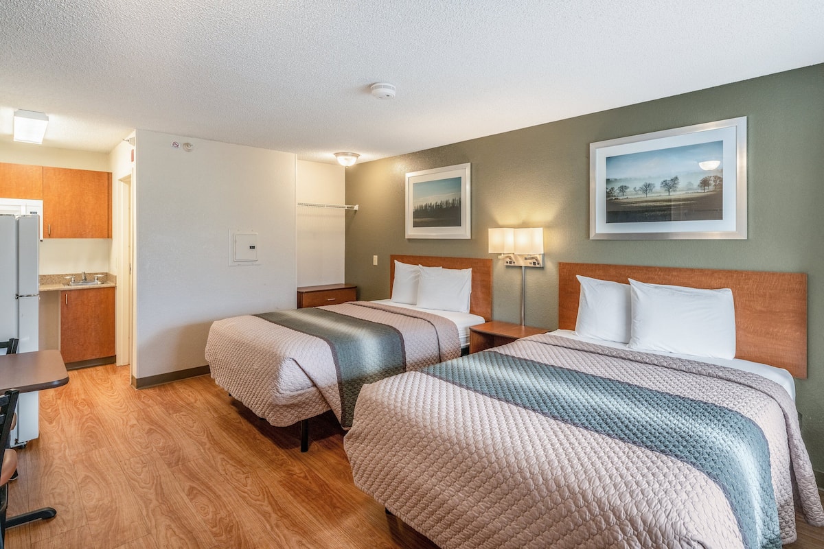 Una habitación de hotel con dos camas, una kitchenette y un baño.