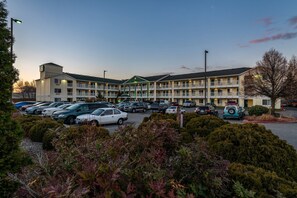 A multi-story motel with a parking lot filled with cars, surrounded by landscaped bushes. - HomeTowne Studios by Red Roof Spokane - Valley (Spokane Valley)
