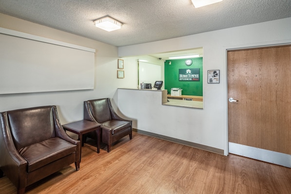 A reception area with two leather chairs, a wooden table, a green wall with a mirror, and a wooden door. - HomeTowne Studios by Red Roof Spokane - Valley (Spokane Valley)