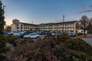 Um motel com vários andares e um estacionamento cheio de carros, rodeado por áreas ajardinadas.