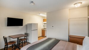 A compact hotel room with a bed, a desk with chairs, a refrigerator, a television, and a small kitchenette. - HomeTowne Studios by Red Roof Spokane - Valley (Spokane Valley)