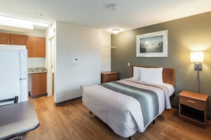 Habitación de hotel con cama, mesitas de noche, escritorio, una silla, kitchenette y un cuadro en la pared.