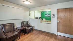 Un espace d’accueil comprenant deux fauteuils en cuir, un comptoir de réception, un mur vert orné d’une enseigne « HomeTownne Studios », une porte en bois et une horloge.