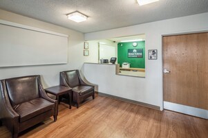 A reception area with two leather chairs, a reception desk, a green wall with a 'HomeTownne Studios' sign, a wooden door, and a clock.