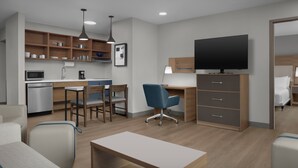 Una habitación de hotel moderna con kitchenette, televisión de pantalla plana, escritorio, silla y cama.