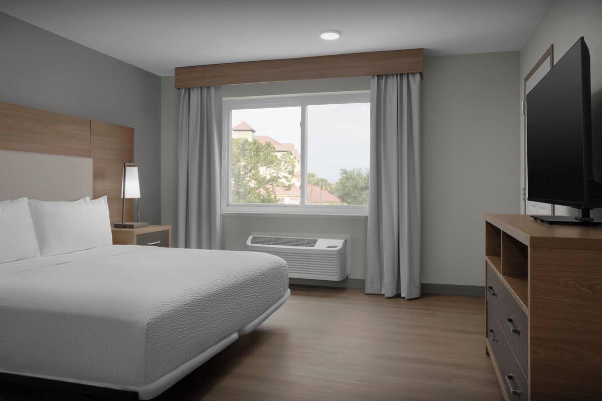 A hotel room with a large bed, a TV, a desk, and a window with curtains.
