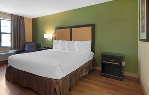 A hotel room with a large bed, a bedside table, a chair, and a window with curtains. - Extended Stay America Select Suites Atlanta Morrow (Morrow)