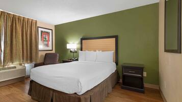 A hotel room with a large bed, a desk, a chair, a nightstand, and a wall-mounted lamp.