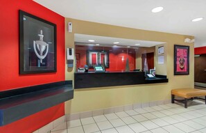 Uma área de recepção com balcão preto, um banco e um quadro na parede.