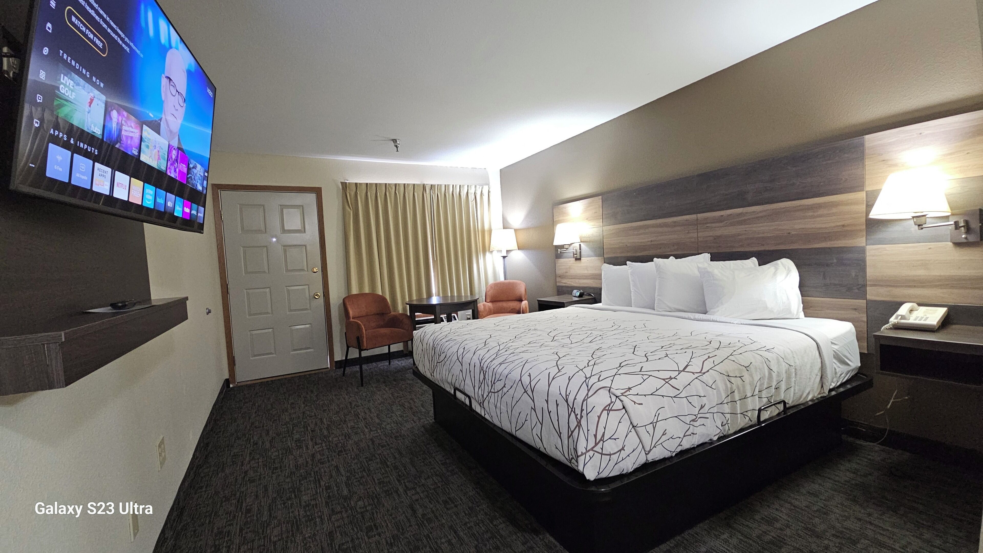 Een hotelkamer met een groot bed, een aan de muur bevestigde televisie, een bureau en een stoel.