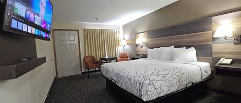 Quarto de hotel com uma cama grande, televisão na parede, escrivaninha e uma cadeira.