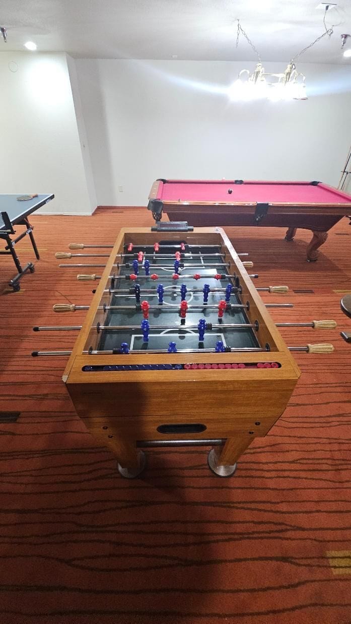 A foosball table in a room with a pool table and a red carpet.