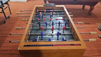 A foosball table in a room with a pool table and a red carpet.