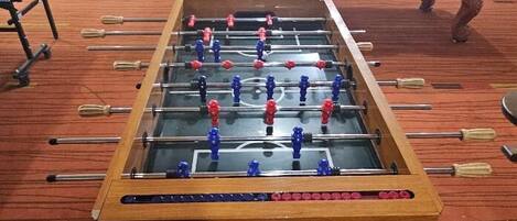 A foosball table in a room with a pool table and a red carpet.