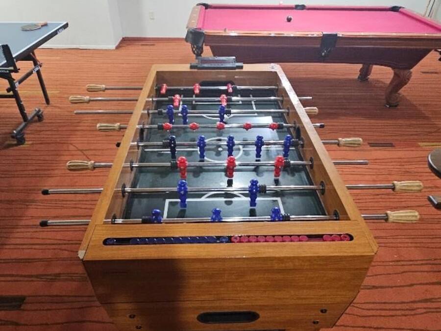 A foosball table in a room with a pool table and a red carpet.