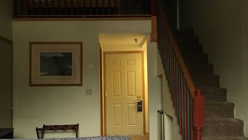 Un dormitorio con una cama, una silla, una puerta y una escalera.
