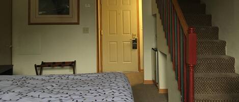 Un dormitorio con una cama, una silla, una puerta y una escalera.