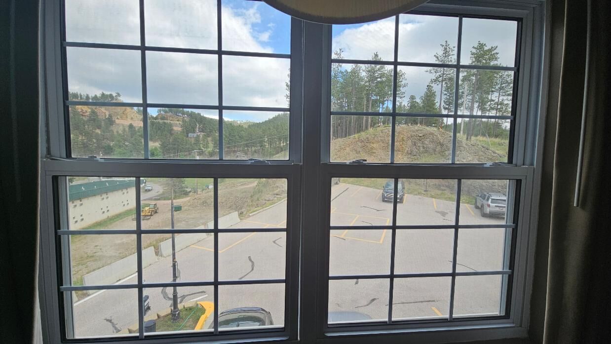 A window with a view of a parking lot and a hilly landscape.
