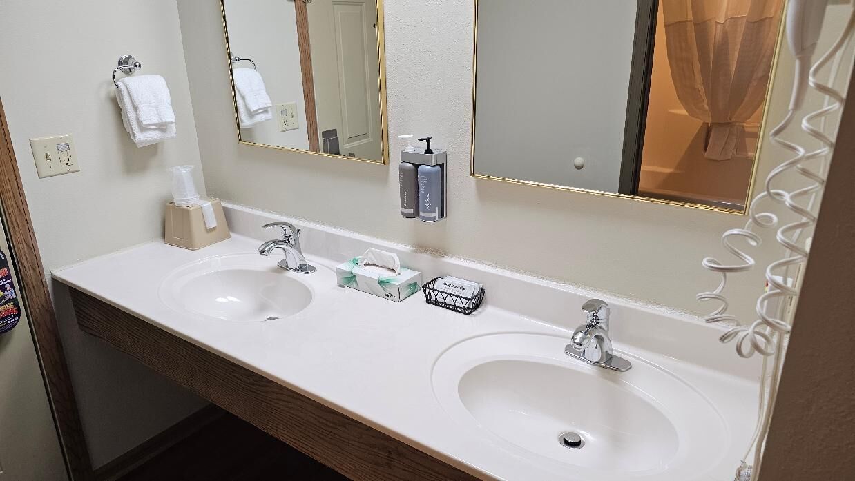 A hotel bathroom with two sinks, a mirror, and a towel rack.