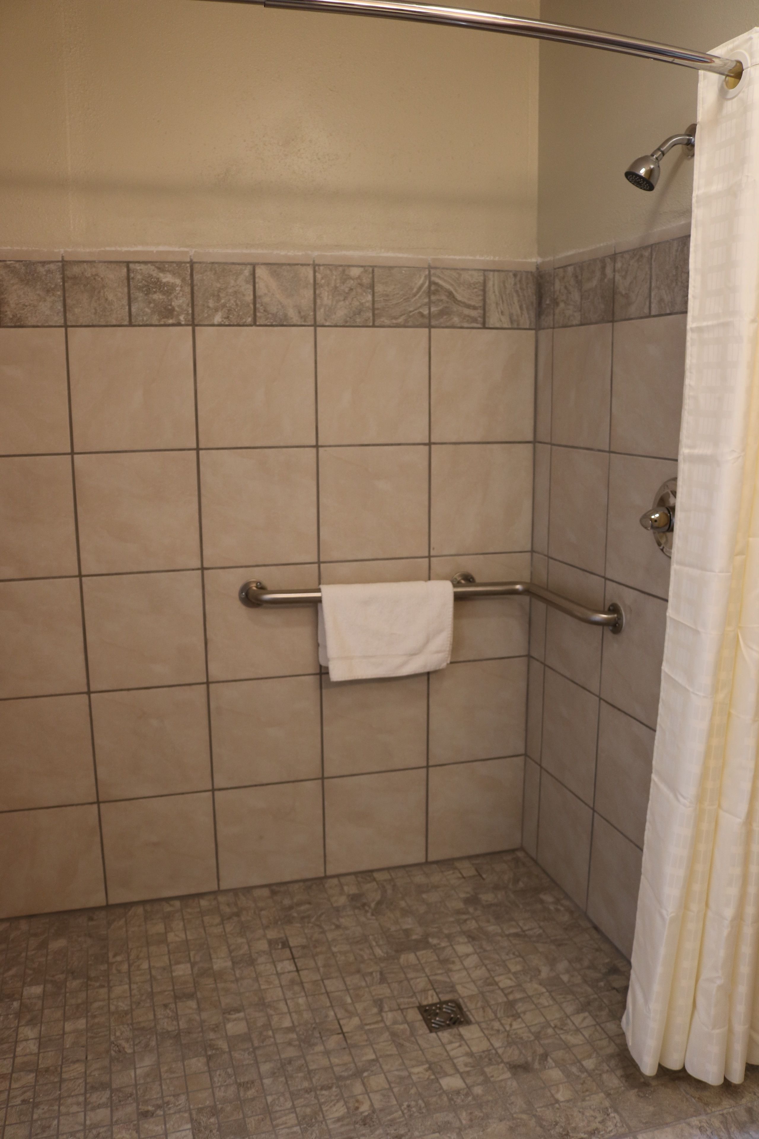 A shower area with a grab bar, a towel rack, and a shower curtain.