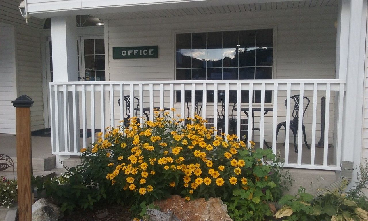 A porch with a white railing, a sign reading "OFFICE", and a row of black chairs.