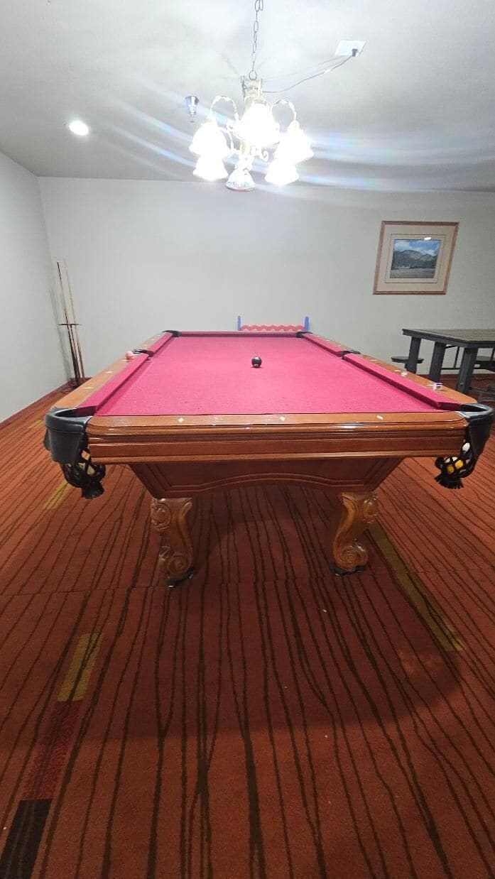 Ein Billardtisch mit roter Spielvliesbahn, umgeben von einem Holzboden mit Streifenmuster.
