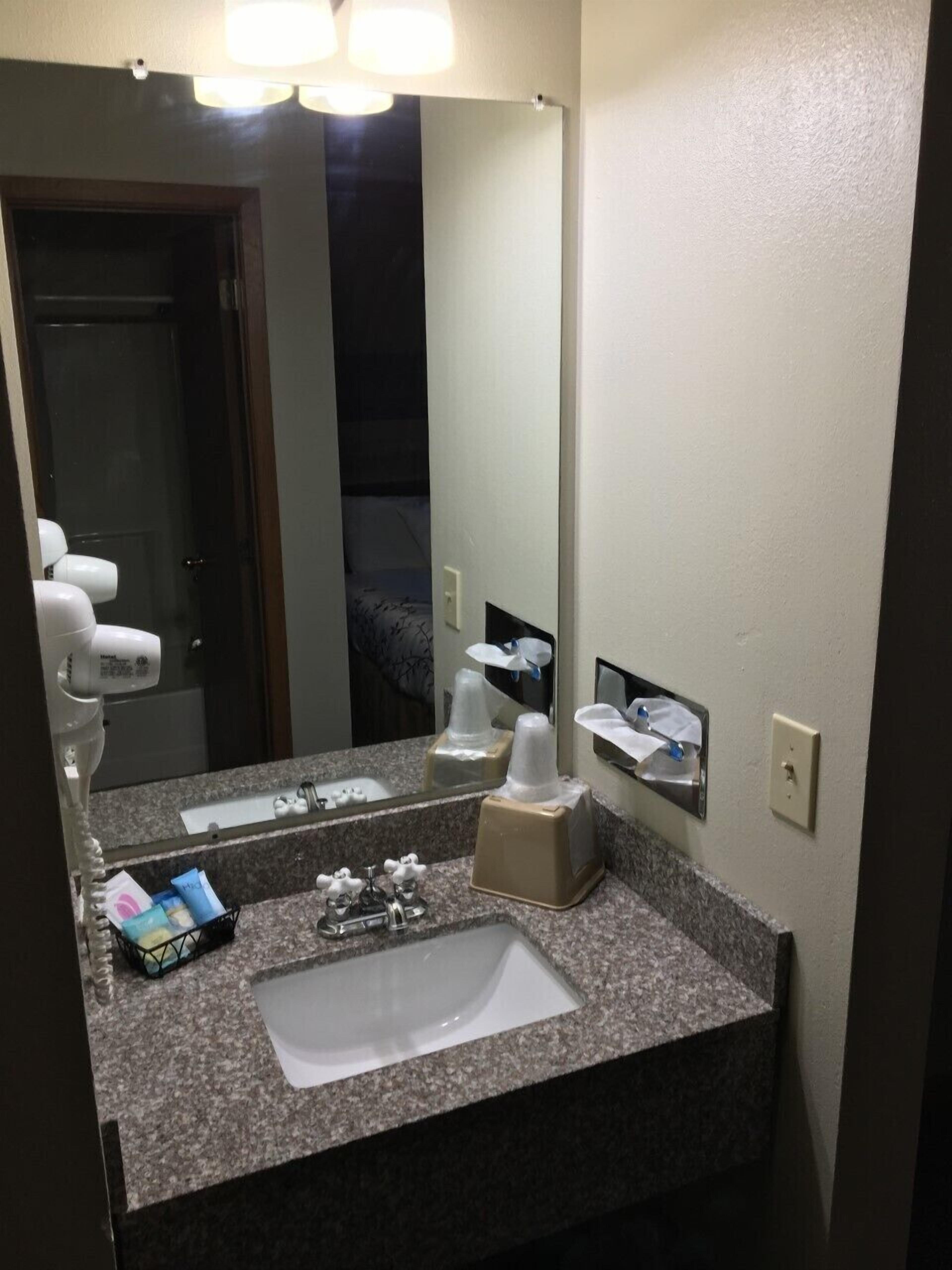 Bagno d'hotel con piano di lavoro in granito, lavandino, specchio, asciugacapelli ed erogatore di fazzoletti.