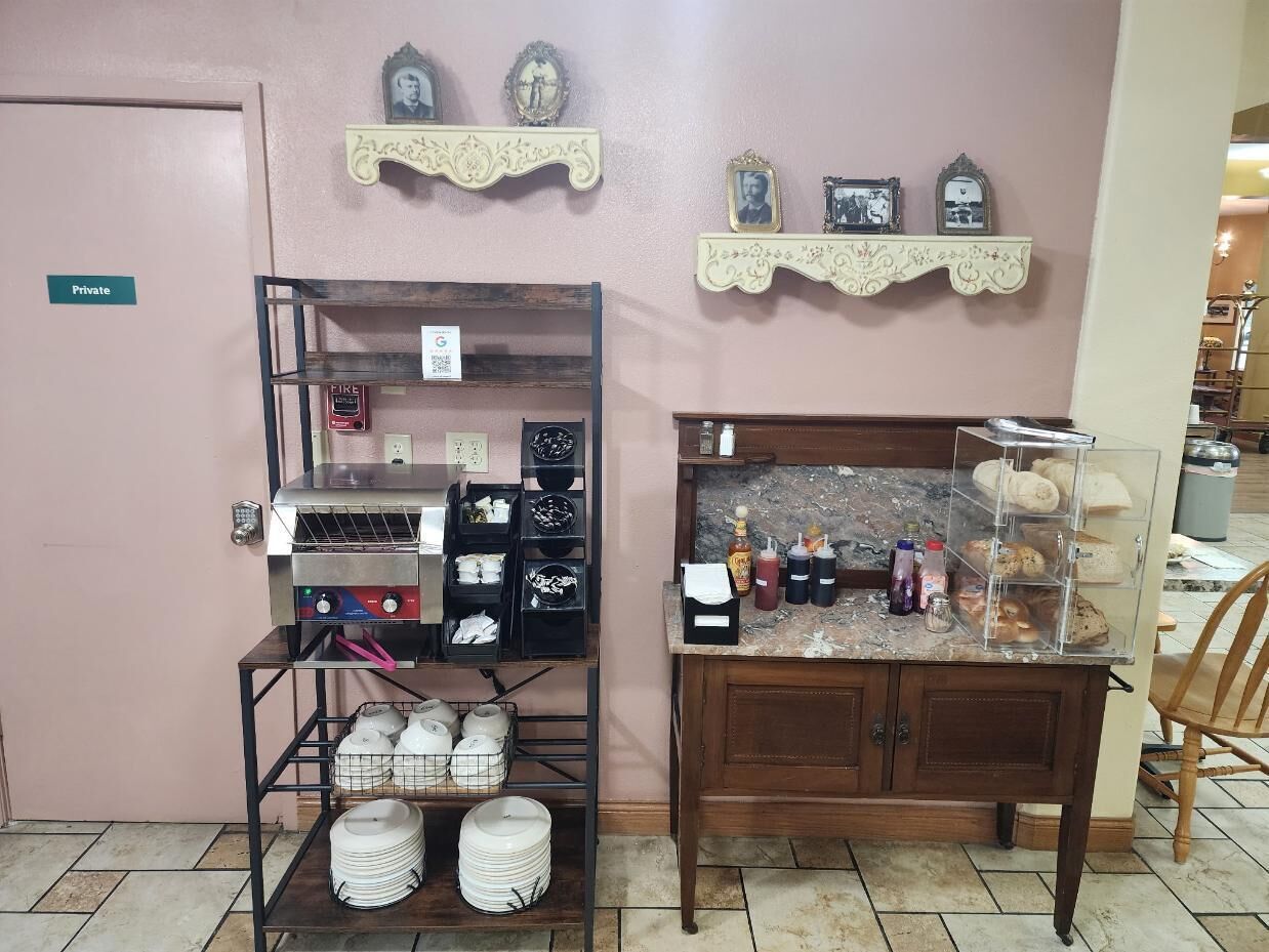 Uma cozinha compacta com fogão, prateleiras com utensílios de cozinha, uma vitrine com produtos de panificação e uma placa indicativa de acesso privado na porta.