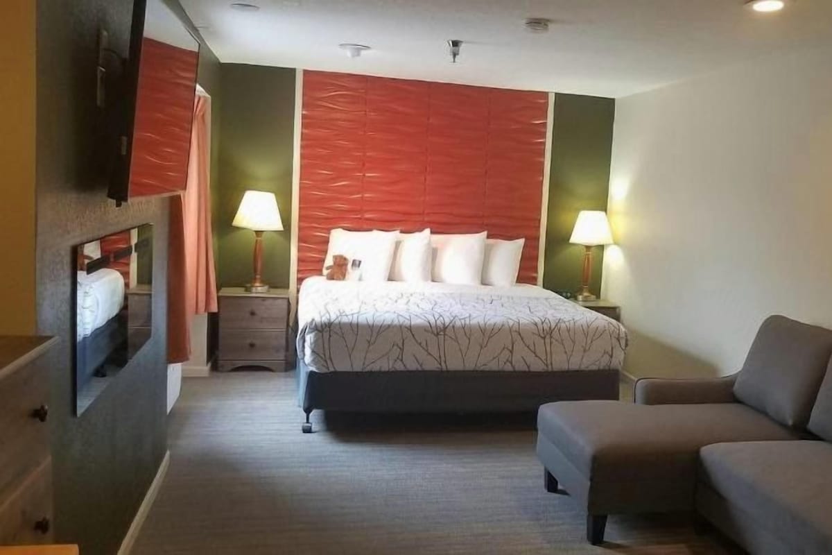 A hotel room with a bed, a sofa, two bedside tables with lamps, and a wall-mounted TV.