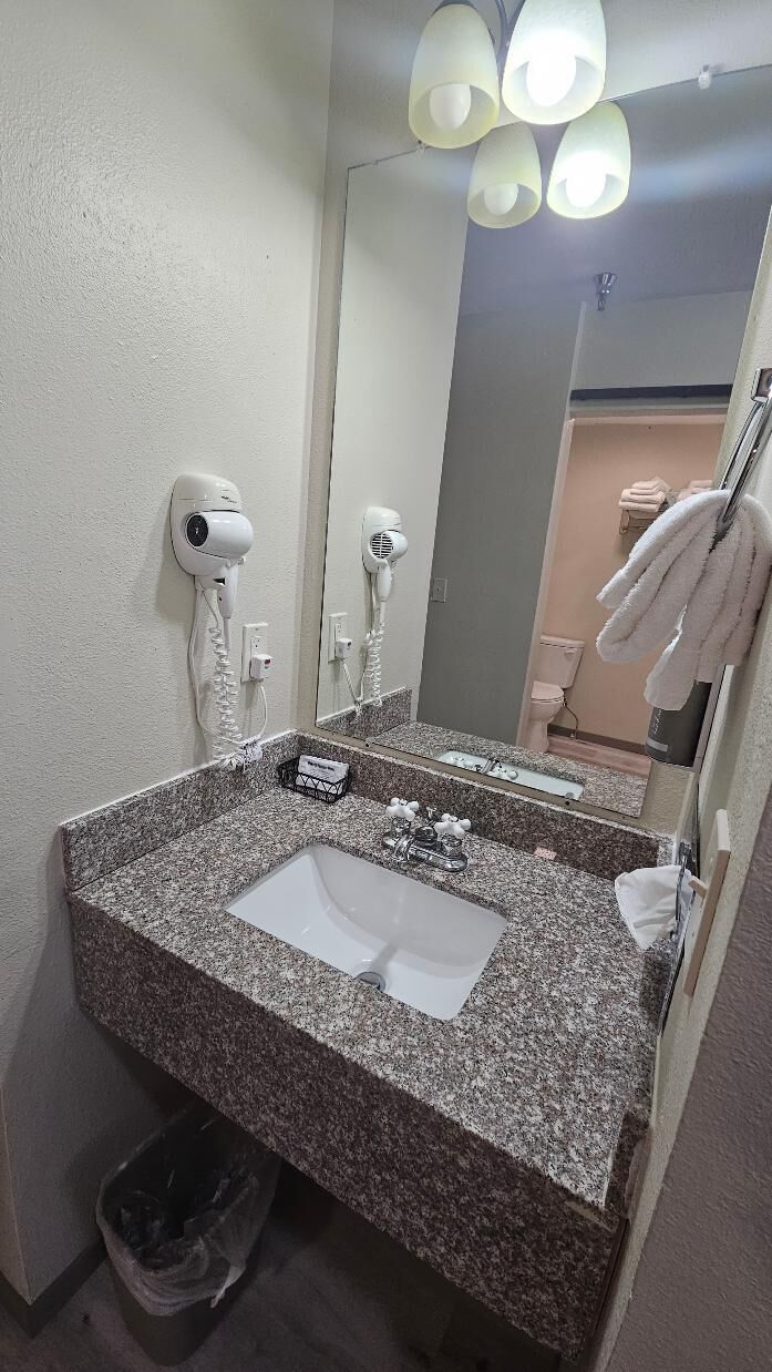Une salle de bain avec un lavabo doté d’un plan de travail en granit, deux sèche-cheveux, un miroir et un porte-serviettes.