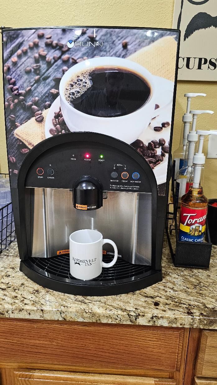 A coffee machine with a cup holder, Torani Classic Caramel syrup, and a coffee cup.