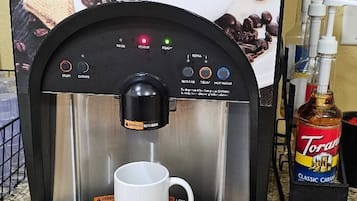 A coffee machine with a cup holder, Torani Classic Caramel syrup, and a coffee cup.