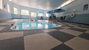 An indoor swimming pool with checkered flooring, poolside chairs, and umbrellas.