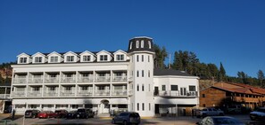 A multi-story hotel with a central tower, multiple balconies, and a parking area with several cars.