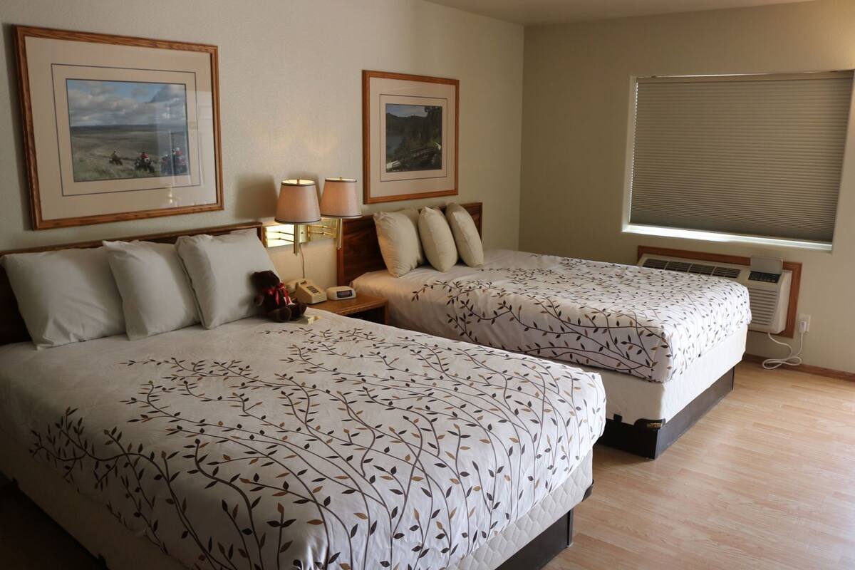 Una habitación de hotel con dos camas, una mesita de noche, una lámpara, un calefactor y cuadros en la pared.