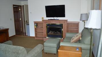 Una sala de estar con un televisor de pantalla plana sobre la chimenea, un sofá verde, una mesa de centro de madera y una lámpara.