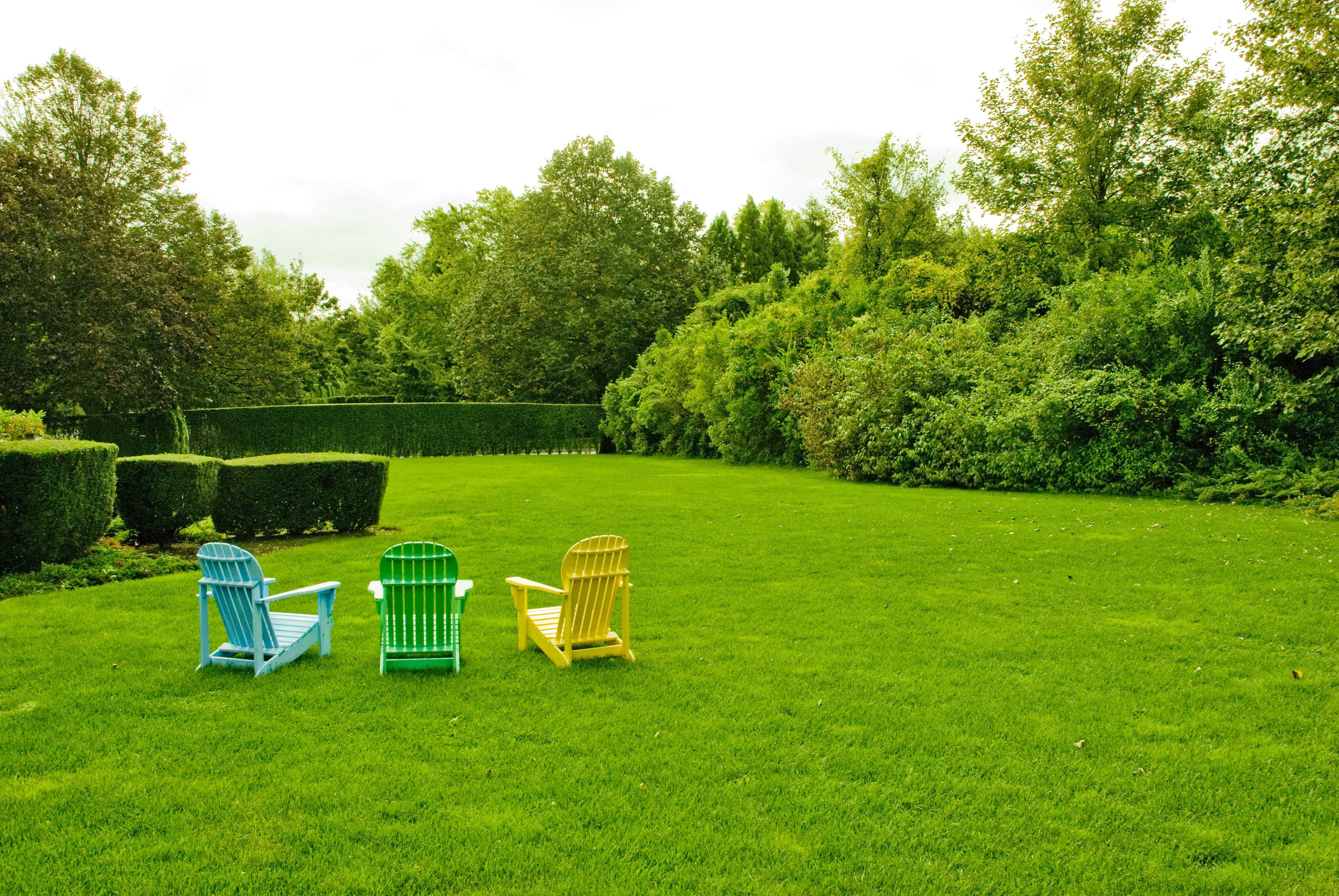 Un espacio al aire libre con césped y tres sillas Adirondack en azul, verde y amarillo.
