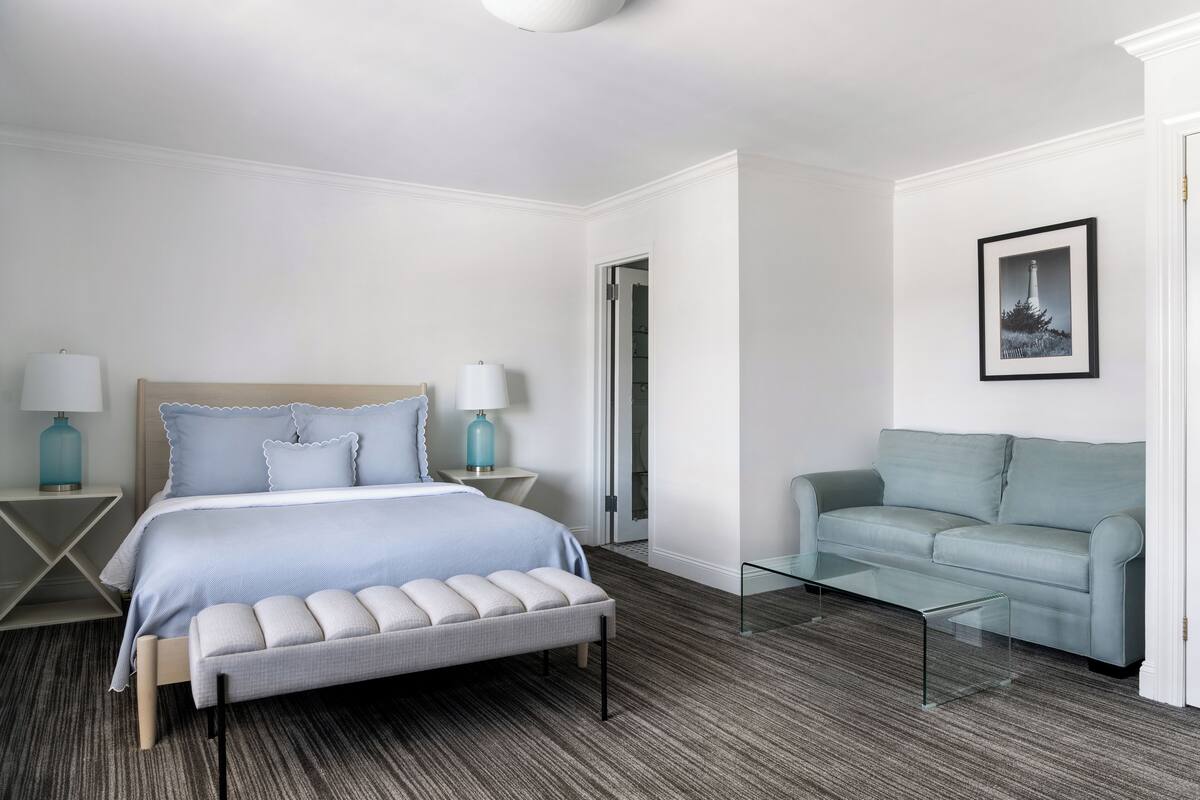 Una habitación de hotel con una cama, una mesa de centro de vidrio, un sofá y un cuadro en la pared.