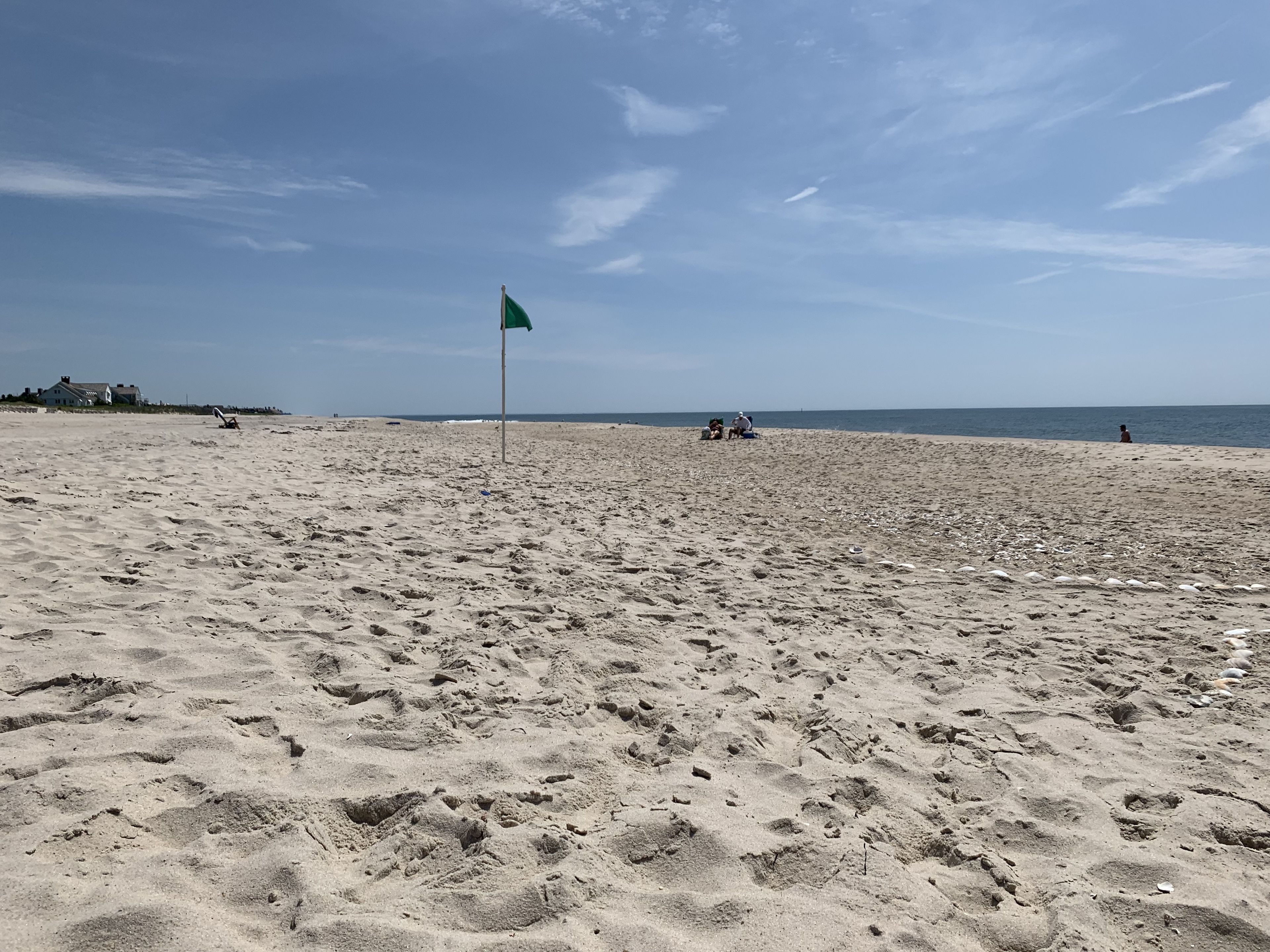 Une plage de sable avec des empreintes de pas, un drapeau vert et quelques personnes au loin.