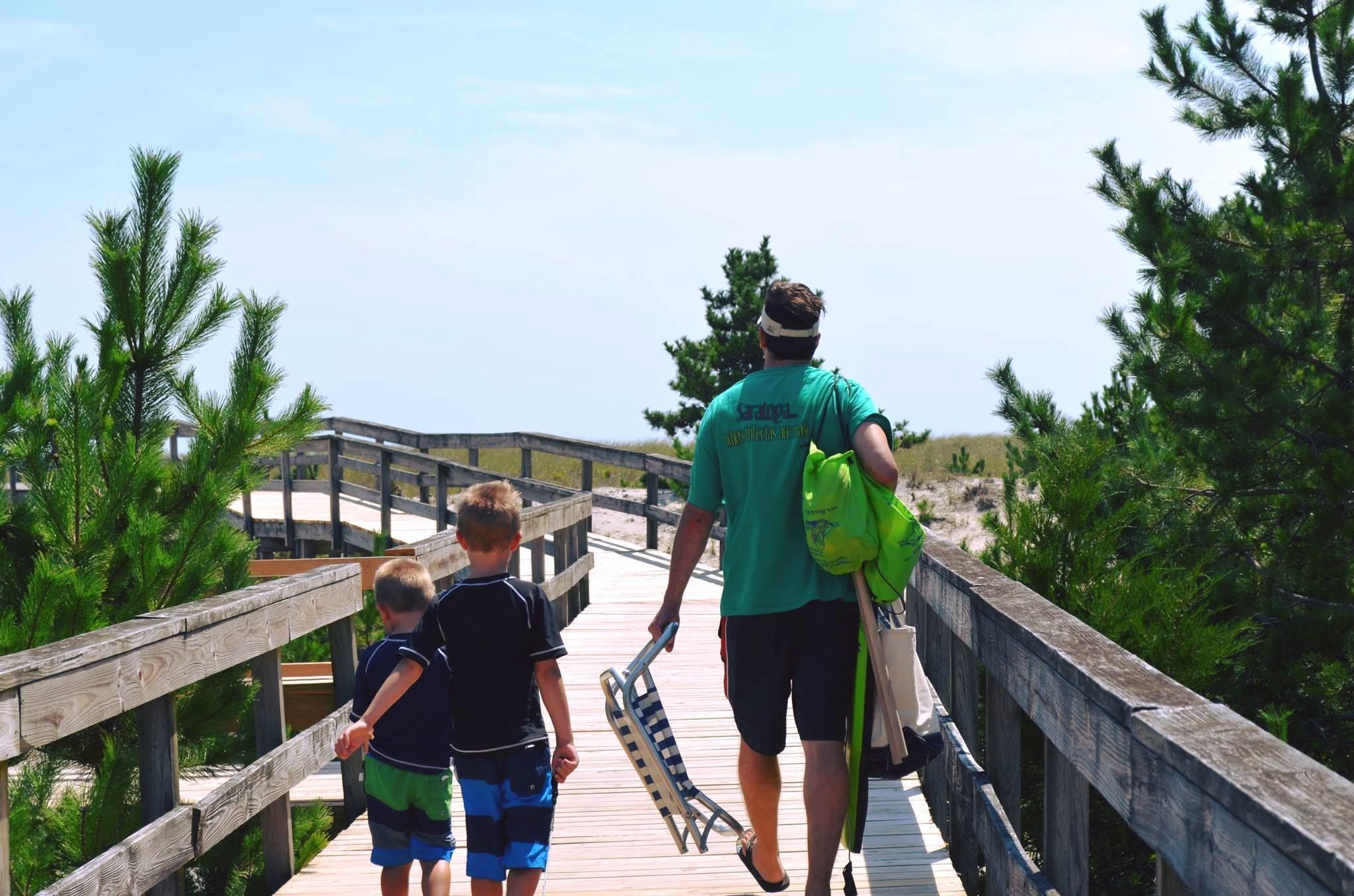 Un paseo marítimo de madera con una persona y dos niños caminando hacia la playa.