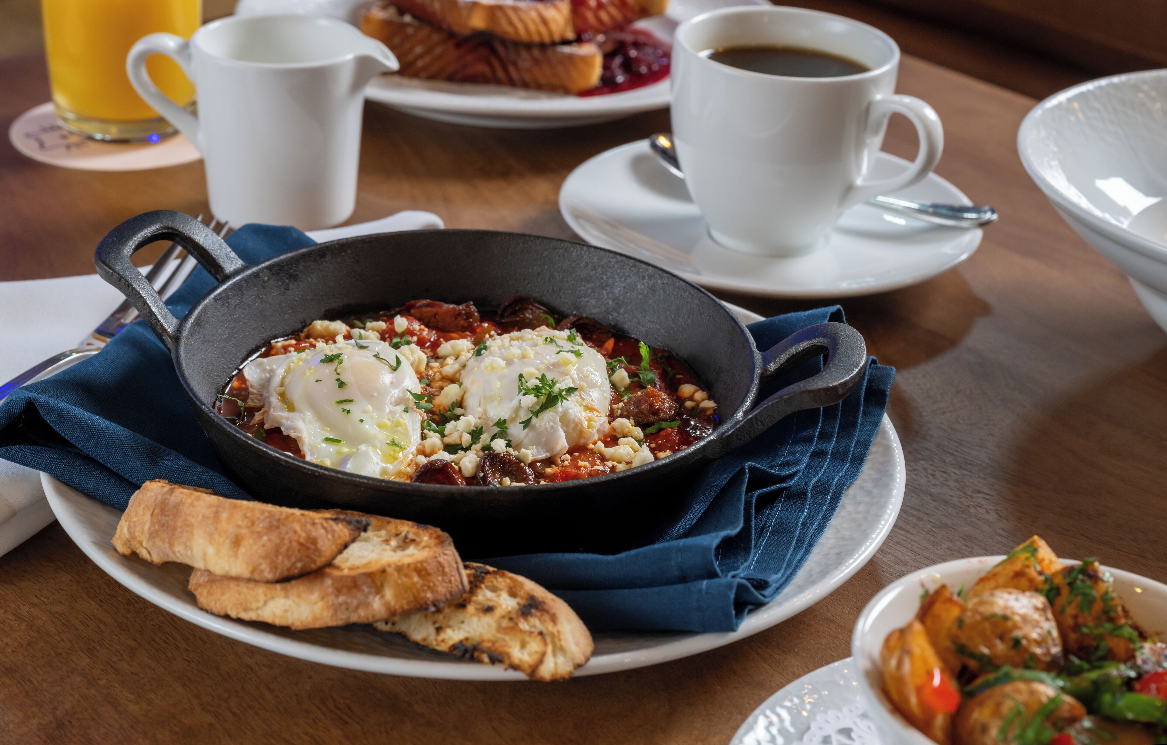 A breakfast setting with a skillet of eggs, toast, and a cup of coffee on a wooden table.