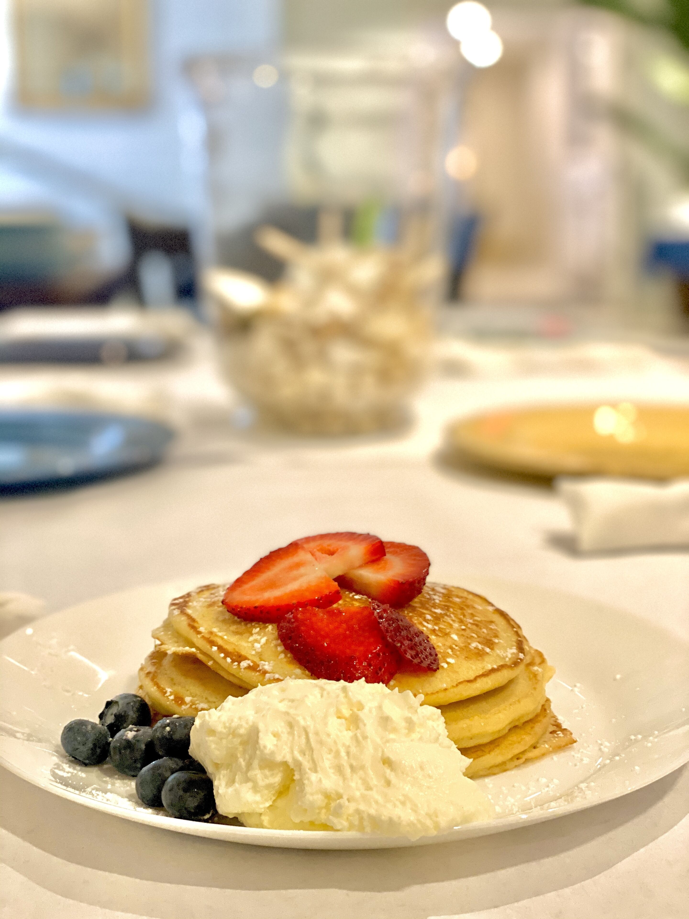 Een stapel pannenkoeken met aardbeien en blauwe bessen, vergezeld van een toef slagroom.